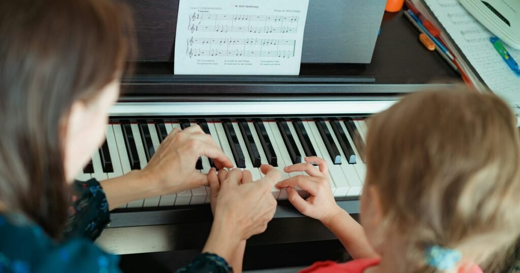Mãe ensina filha a tocar piano lendo partitura, retratando o cuidado clínico da musicoterapia