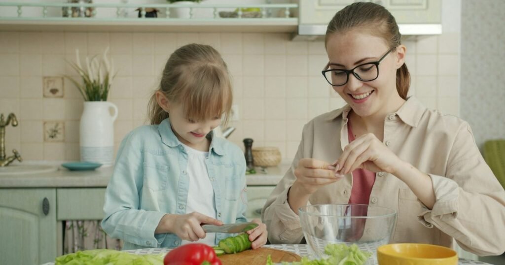 Mãe e filha preparam salada juntas na cozinha, simbolizando a nutrição pediátrica e o combate à obesidade infantil